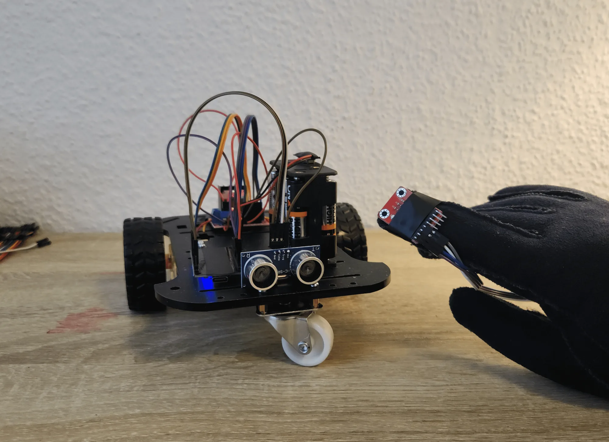 Gloved hand with a motion sensor on the index finger, held up to the two-wheel robot it steers