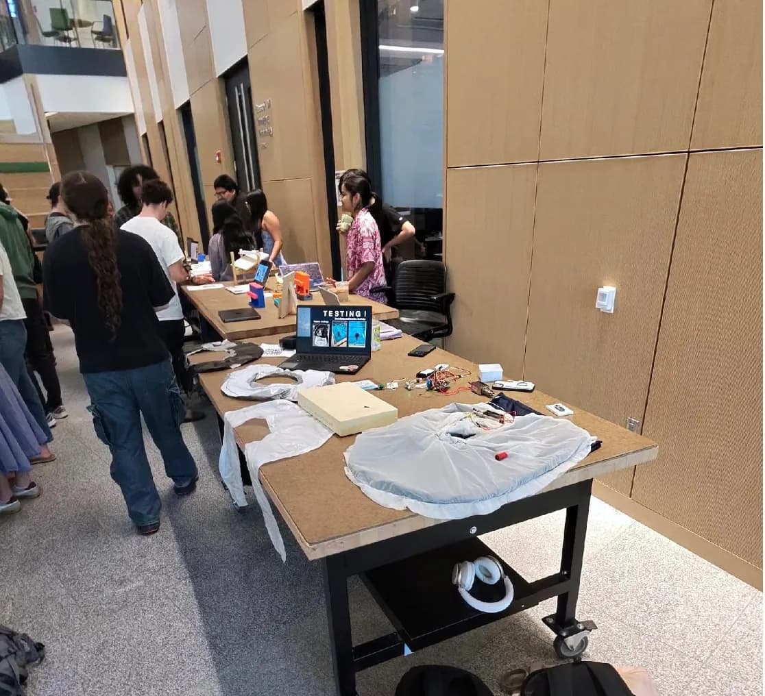 The SwimSafe prototype on the bench at the ENGS 21 showcase: a garment with wiring and sensors laid out, a laptop beside it running the test slides